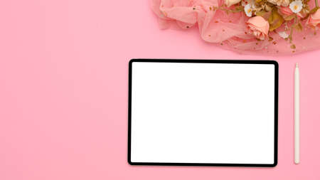 Top view, flat lay, Female workspace with portable tablet computer white display with stylus pen, flower bouquet and copy space on pink background.の写真素材