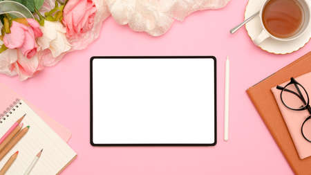 Stylish pink female office workspace top view with digital tablet white screen mockup, roses bouquet, a cup of tea and stationery. flat layの写真素材
