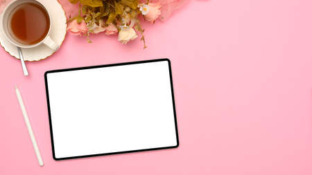 A modern pink office workspace top view with a mockup screen of digital tablet touchpad, a cup of tea and flowers on pink background.の写真素材