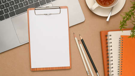 Minimal office table workspace with empty paper on wooden clipboard over laptop keyboard, pencils,...