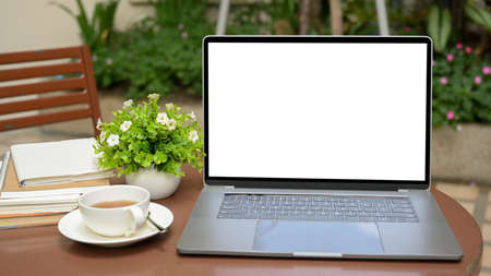 Close-up, A portable outdoor workspace with portable laptop computer white screen mockup, a cup of tea and decor on wooden coffee table.の写真素材