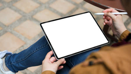 A female college student using a portable tablet computer with stylus pen, sitting in the garden.