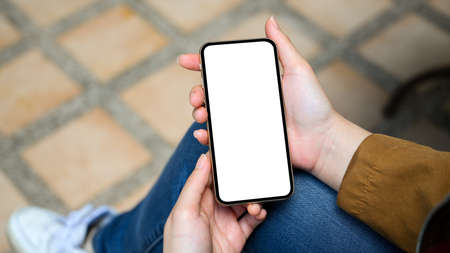 Female sitting in the park, enjoying her weekend and relaxing on her mobile application. Close-up, smartphone white screen in a woman's hands.の写真素材