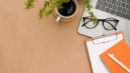 Brown workspace table background with copy space for product display, coffee cup, eyeglasses, clipboard paper, laptop computer and notepad. top view, flat layの写真素材