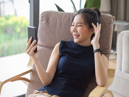 Happy Asian young woman spend her day off at home, enjoy video call with her friends in living room.