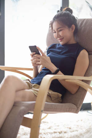 Portrait, Attractive Asian teen woman sits in modern and comfy armchair in bright living room, using...