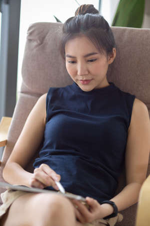 Portrait, Beautiful female relaxes in her home living room, sits at her comfortable armchair and using digital tablet.の写真素材