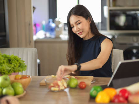 Healthy Asian young woman preparing fruits and vegetables for her healthy drink and salad in the kitchen. Home cooking conceptの写真素材