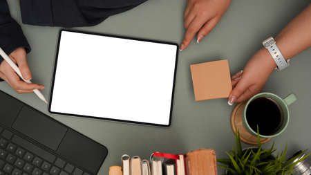 Two businesswomen discussing plan on digital tablet and working together in modern office desk. Tablet blank screen mockup, sticky notes, stationery and supplies. top viewの写真素材