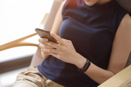 Close-up image, Relaxed female sits in comfy armchair and using smartphone in the living room.の写真素材
