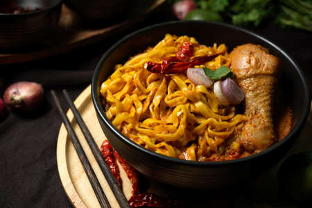 Khao Soi Kai, Tasty and spicy creamy yellow curry noodles with chicken drumstick in black bowl served with chopsticks. Thai northern cuisine.の写真素材