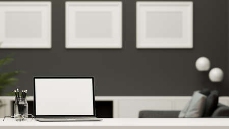 Modern contemporary home office desk with portable laptop white screen mockup, pencils, glasses and copy space on tabletop over blurred living room in the background. 3d rendering, 3d illustrationの写真素材