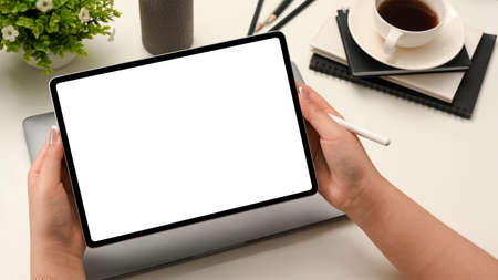 Female hand holding a digital portable tablet touchpad computer white empty screen mockup and stylus...