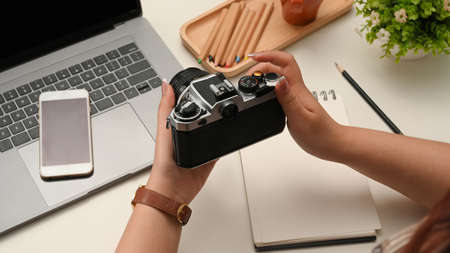 Close-up image, Female hands holding a retro camera over her modern office desk. photographer, blogger, freelancerの写真素材