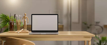 Minimal cozy home office workspace with laptop white screen mockup, decor and painting tools on wooden table over blurred living room background. 3d rendering, 3d illustrationの写真素材