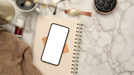 Minimal cozy feminine working space with smartphone blank screen mockup, spiral notepad, brown sweater and accessories on marble white background. top viewの写真素材