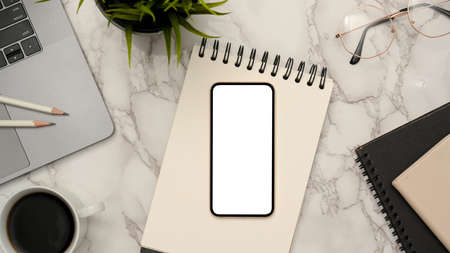 Trendy office workspace top view with laptop, coffee cup, pencils, notepad, decor plant and smartphone white screen mockup. flat layの写真素材