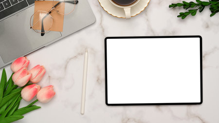 Top view, Feminine office desk workspace in white marble background with digital tablet white screen mockup, tulips flowers, laptop, glasses and decor.の写真素材