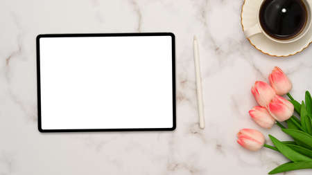 Overhead shot, White marble background with tablet touchpad blank screen mockup, stylus pen, coffee cup and tulips flower. clipping path, flat layの写真素材