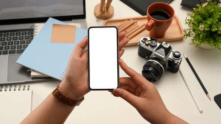 A smartphone white screen mockup for display your graphic banner in a woman's hand over office desk.の写真素材