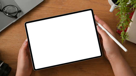 Overhead shot, Graphic designer using digital tablet touchpad white screen mockup on wooden table.