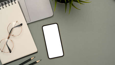 Modern study table with smartphone white screen mockup, eyeglasses, laptop, school notebook, pencil and copy space on grey background. top view, flat layの写真素材