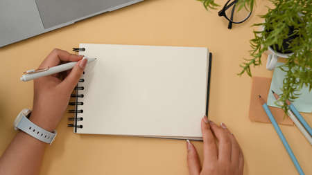 Female university student taking notes on spiral notepad, writing a greeting card on her workspace. Empty spiral notepad mockup. top viewの写真素材