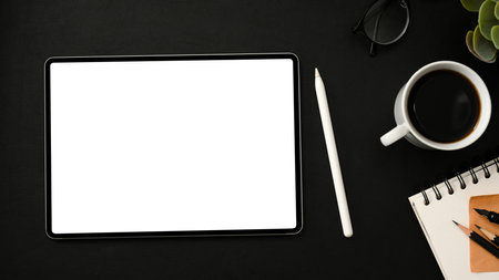 Overhead shot, Dark modern workplace with portable touchpad white screen mockup, stylus pen, a cup of coffee and stationery on black background.の写真素材