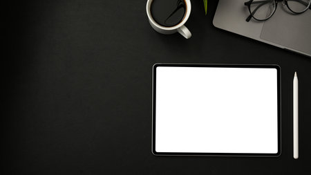 Top view, Modern business office desk with portable tablet touchpad white screen mockup, stylus pen, coffee cup, eyeglasses, laptop and copy space on black background.の写真素材