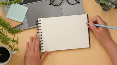 Female officer wiring her ideas on spiral notepad in her minimal office desk. Empty spiral notepad mockup. top viewの写真素材