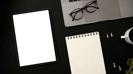 Creative stylish dark office desk workspace with portable tablet white screen mockup, empty spiral...