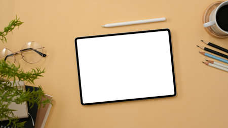 Workspace top view with digital tablet touchpad white screen mockup, pencils, coffee cup and decor on beige background.の写真素材