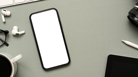 Modern grey office desk background with cellphone white screen mockup, earbuds, copy space and accessories. top viewの写真素材