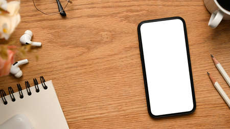 Top view, Simple workspace with cellphone white screen mockup, pencils, spiral notepad, earbuds and...