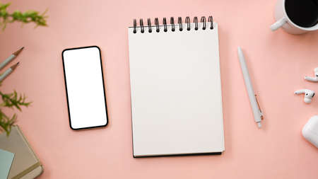 Top view, Pink office desk background with empty spiral notepad, office accessories and smartphone...