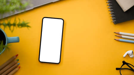 Creative workspace table with smartphone white screen mockup, office accessories and copy space on yellow background. top view, flat layの写真素材