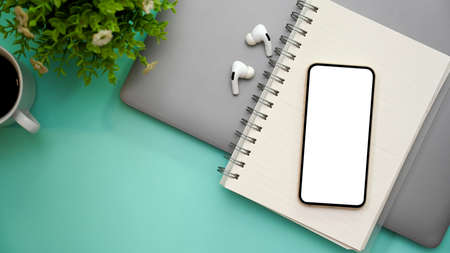 Stylish light green workspace background with laptop computer, earbuds, spiral notebook, coffee cup,...