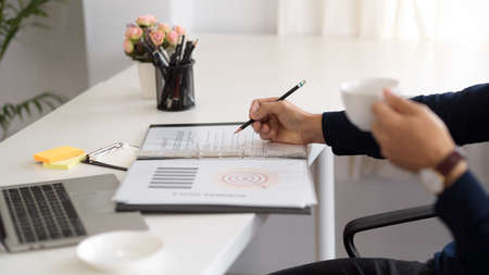 Cropped shot of a businessman drinking coffee and examining his financial business data on the...