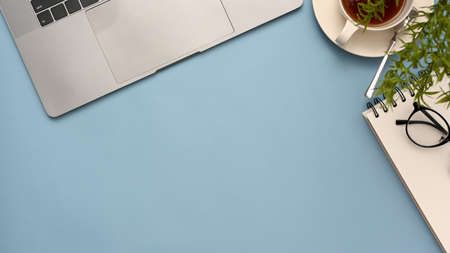 Office tabletop workspace in blue background with notebook laptop, coffee cup, notepad, glasses and copy space. top view, flat layの写真素材