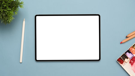 Creative workspace top view with tablet white screen mockup for display your graphic, stylus pen, water colour palette and stuff on blue background.の写真素材