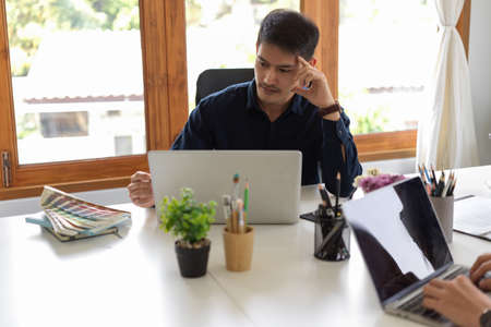 Stressed Asian businessman in the formal meeting, looking something at laptop screen and pensive thinking the new idea.の写真素材