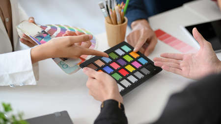 Cropped, closeup, Group of graphic designers pointing their fingers on colour swatches samples over...