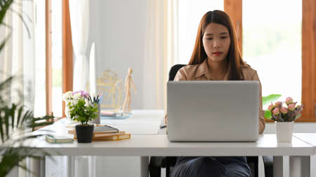 Asian young businesswoman or female worker using laptop computer in her modern office workplace.