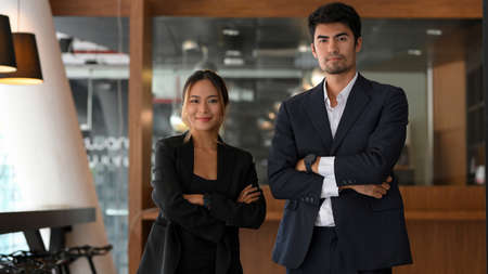 Confident and successful Asian young businesswomen and businessmen in formal suits stand with their arms folded in their office.の写真素材