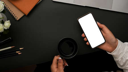 Close-up, top view, Relaxed female drinking coffee while using smartphone over her modern black...
