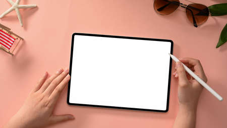 A female freelancer's hands use a stylus to design a graphic image on a tablet screen against a...