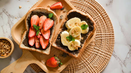 Top view, Healthy toasts, Strawberry and banana with dark chocolate spread on whole grain bread on wooden plate.の写真素材
