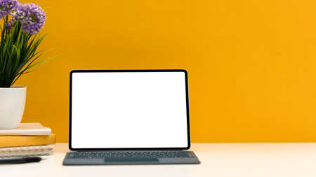 Creative stylish workspace with portable tablet touchpad white screen mockup stand on wireless keyboard on white table over yellow background. close-upの写真素材