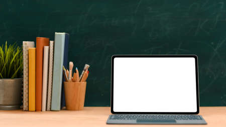 Education space concept, Laptop computer white screen mockup for montage your graphic on screen, stack of books, decor plant and stationery against green chalkboard background.の写真素材