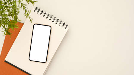 Top view, flat lay, Smartphone blank empty screen mockup, spiral notepad, plant and copy space on white background.の写真素材